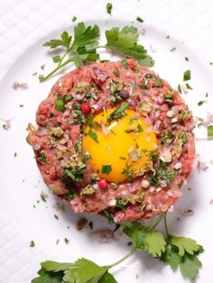 a white plate topped with an egg on top of meat and garnished with parsley