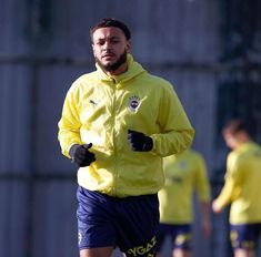 a man running on a field with other men in the background wearing yellow jackets and blue shorts