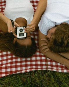 two people laying on a red and white checkered blanket with an old fashioned camera