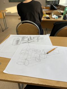 a person sitting at a table with two drawings on it and a pen in front of them