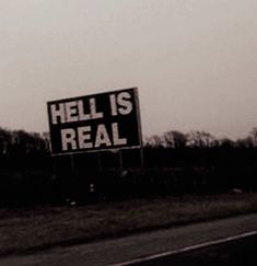 a sign that reads hell is real on the side of a road in front of trees