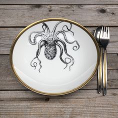 a plate with an octopus drawn on it next to a fork and knife sitting on a wooden table