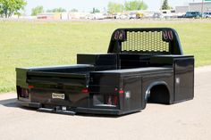 a black truck parked on the side of a road next to a grass covered field