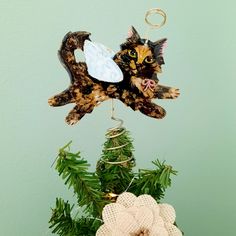 a cat ornament hanging from a tree with pine cones on the bottom and green wall behind it