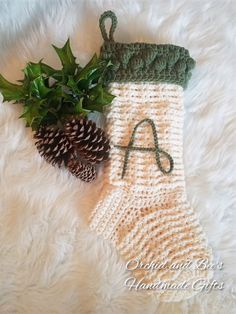 a crocheted stocking with the letter a on it next to a pine cone