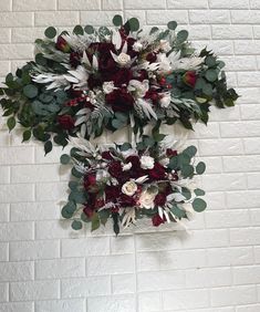 two white and red flowers hanging on a brick wall with greenery in the center