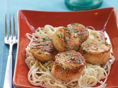 some scallops are sitting on top of spaghetti in a red bowl next to a fork