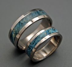 two wedding bands with blue marble inlays are shown on a gray surface,