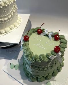 a green cake sitting on top of a table next to a plate with two cherries