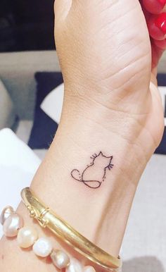 a woman's wrist with a cat tattoo on it and pearls around the wrist