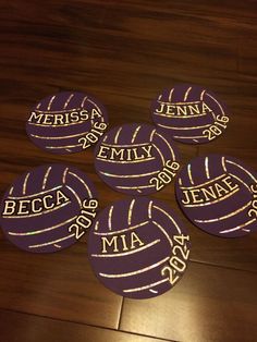 four personalized volleyball coasters on a wooden floor with purple and gold foiling