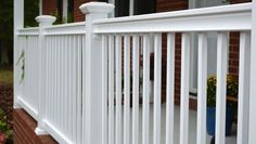 a close up of a white railing on a brick house with flowers in the foreground