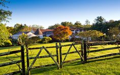 a wooden fence in front of a green field with houses and trees on the other side