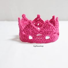 a crocheted pink crown sits on a white surface