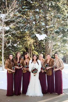 a group of women standing next to each other in front of snow covered trees and holding bouquets