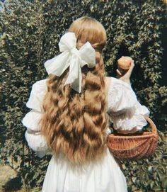 a girl with long hair and a bow holding an apple in front of some bushes