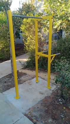 a yellow metal structure sitting in the middle of a yard next to bushes and trees