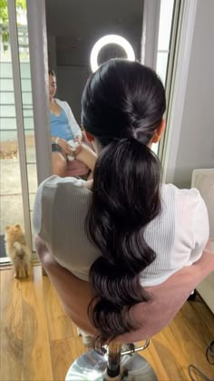 a woman sitting in front of a mirror with her hair styled into a pony tail