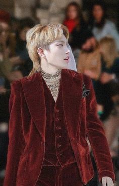 a man in a red velvet suit and silver necklace walking down the runway at a fashion show