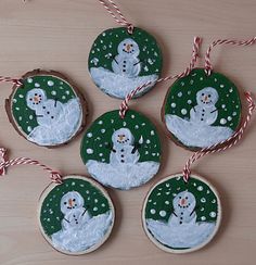 four snowman ornaments are hanging from twine on a wooden table with candy canes