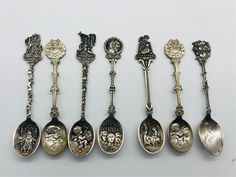 six antique spoons are lined up on a white surface, each with different designs