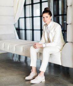 a woman in a white suit sitting on a bench with her legs crossed and feet crossed