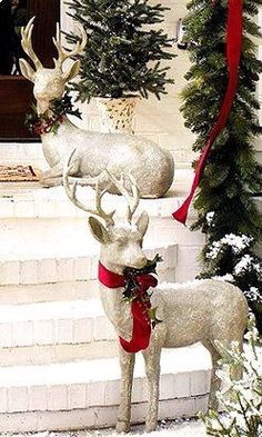 two white deer statues with red bows on their antlers in front of a house