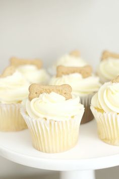 cupcakes with white frosting and bows on them are sitting on a cake plate