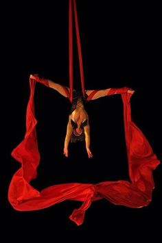 a woman is suspended upside down in the air on a red cloth with her legs spread out