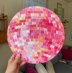 a person holding up a pink and orange mosaic paper plate