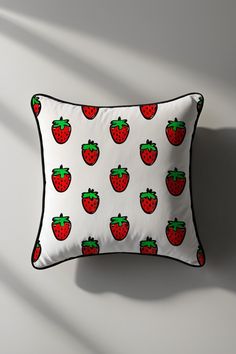 a white pillow with red strawberries on it and green leaves in the middle, against a gray wall