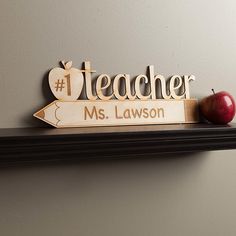 a wooden teacher sign sitting on top of a shelf with an apple next to it