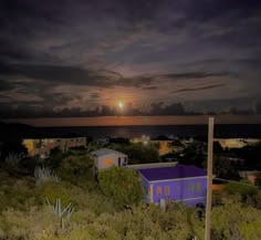 the sun is setting over some houses and trees in front of an ocean with dark clouds