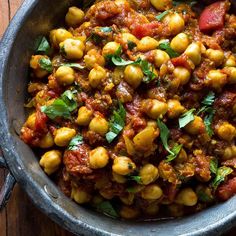 a pan filled with chickpeas and sauce on top of a wooden table