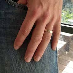 a person wearing a gold ring on their left hand and blue jeans with trees in the background