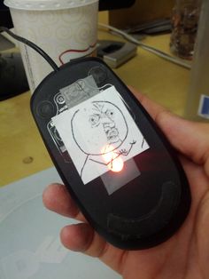 a person holding up a computer mouse with a sticker on it's face