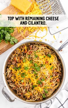 a pan filled with spaghetti and cheese on top of a table next to parmesan cheese