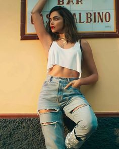 a woman in ripped jeans leaning against a wall