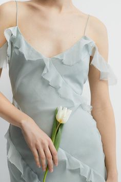 a woman in a gray dress holding a white flower with her right hand on the side