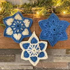 two crocheted snowflakes hanging from a wood plank with christmas lights in the background