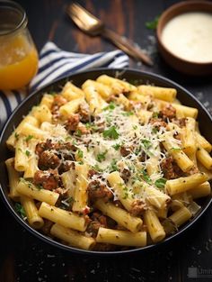 pasta with sausage and parmesan cheese in a black bowl on a wooden table