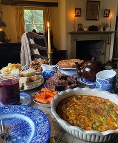 a table filled with plates and bowls full of food next to a fireplace in a living room