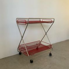 a metal cart with two red baskets on it's top and bottom wheels, against a white wall