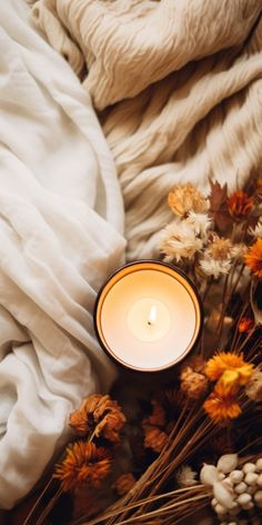 a white candle sitting on top of a bed next to dried flowers