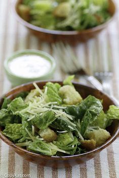 two bowls filled with green vegetables on top of a striped table cloth next to silverware