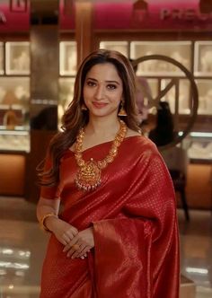 a woman in a red sari and gold necklace standing with her hands on her hips