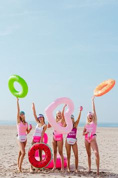 four women in pink bathing suits holding up frisbees on the beach