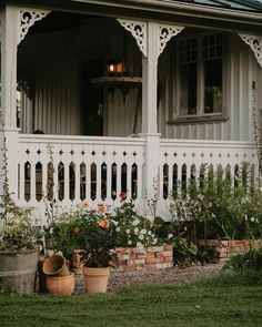 the front porch of a white house with potted plants and flowers on the lawn