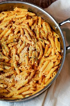 a pan filled with pasta and sauce on top of a white cloth next to a wooden table