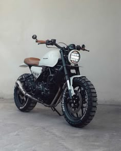 a white and black motorcycle parked in front of a gray wall with a wooden handlebar